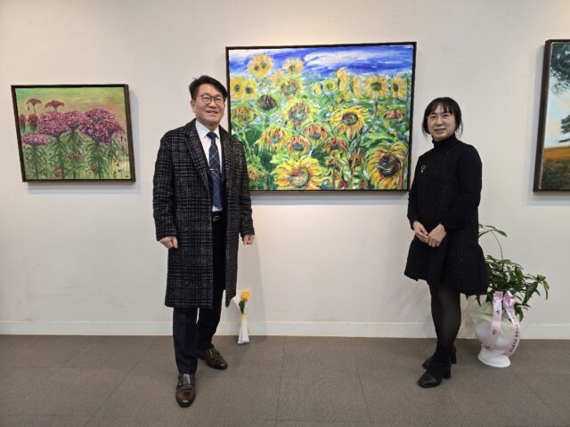 고건필 작가(왼쪽)와 그의 부인이 첫 개인전 ‘비로소, 나를 그리다’가 열리고 있는 부여문화원 전시실에서 해바라기 작품을 배경으로 기념 촬영을 하고 있다.