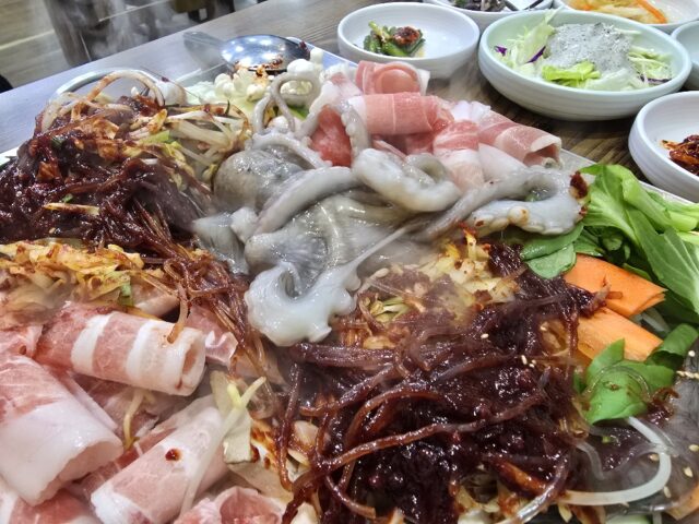 “육(肉)과 해(海)의 만남” 철판 위에서 주인공인 낙지가 투입되어 익어가는 모습. 매콤한 특제 양념이 배어들며 삼겹살의 고소함과 해산물의 감칠맛이 하나로 어우러지기 시작한다.