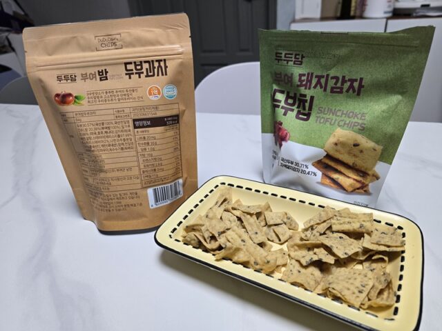 부여군 남면에서 생산된 '부여 밤 두부과자'와 '부여 돼지감자 두부칩'의 패키지 모습. 세련된 색감의 전면 디자인과 상세한 영양 정보가 담긴 후면이 정갈한 가정집 식탁 위에서 조화를 이루고 있다.