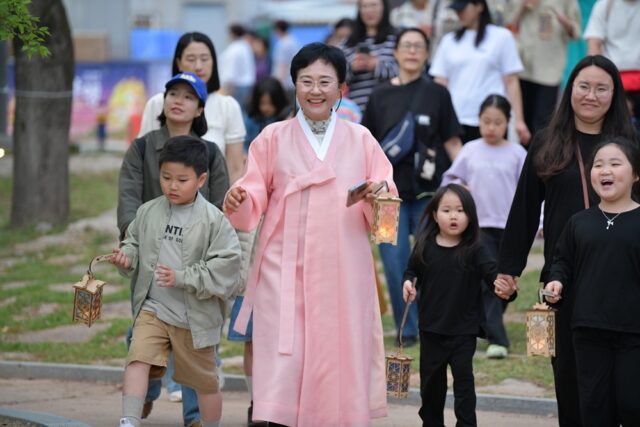 '2026 부여 국가유산 야행'에 참가한 어린이와 학부모들이 부여향교에서 선비체험을 마친 뒤, 한복을 입은 강사의 안내에 따라 각자의 소망을 담은 나무 연등을 들고 '탑돌이' 행사가 열리는 정림사지 오층석탑으로 이동하고 있다.